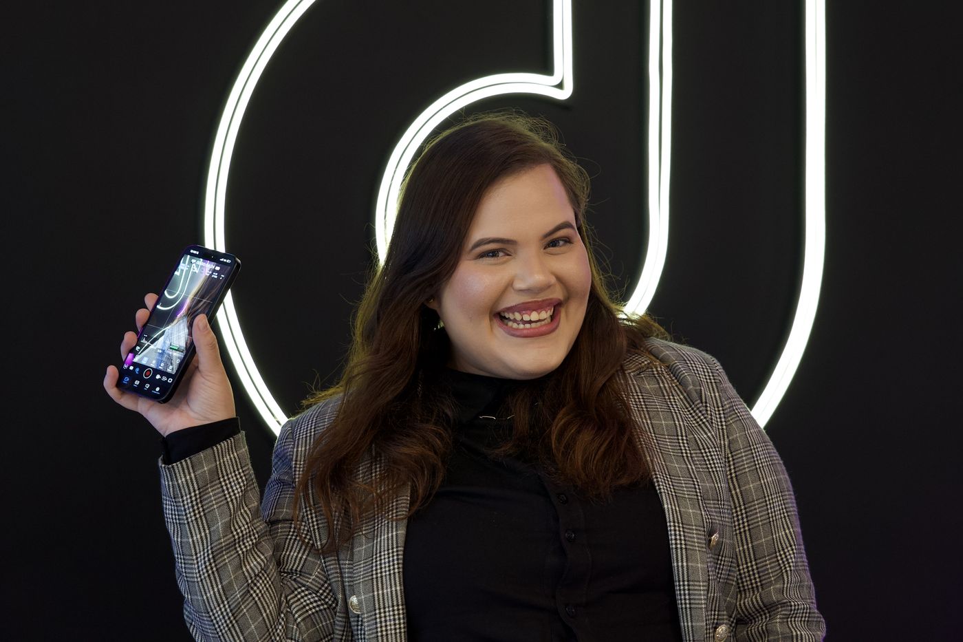 Integrante da Agniz Films com o celular, em frente ao logo em neon